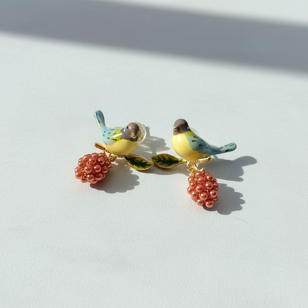 Pair of bird-shaped earrings with pink berry-like charms on a white background