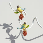 Pair of earrings with bird and berry design on a white background