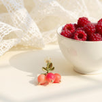 Bowl of raspberries with a pair of earrings on a white lace background