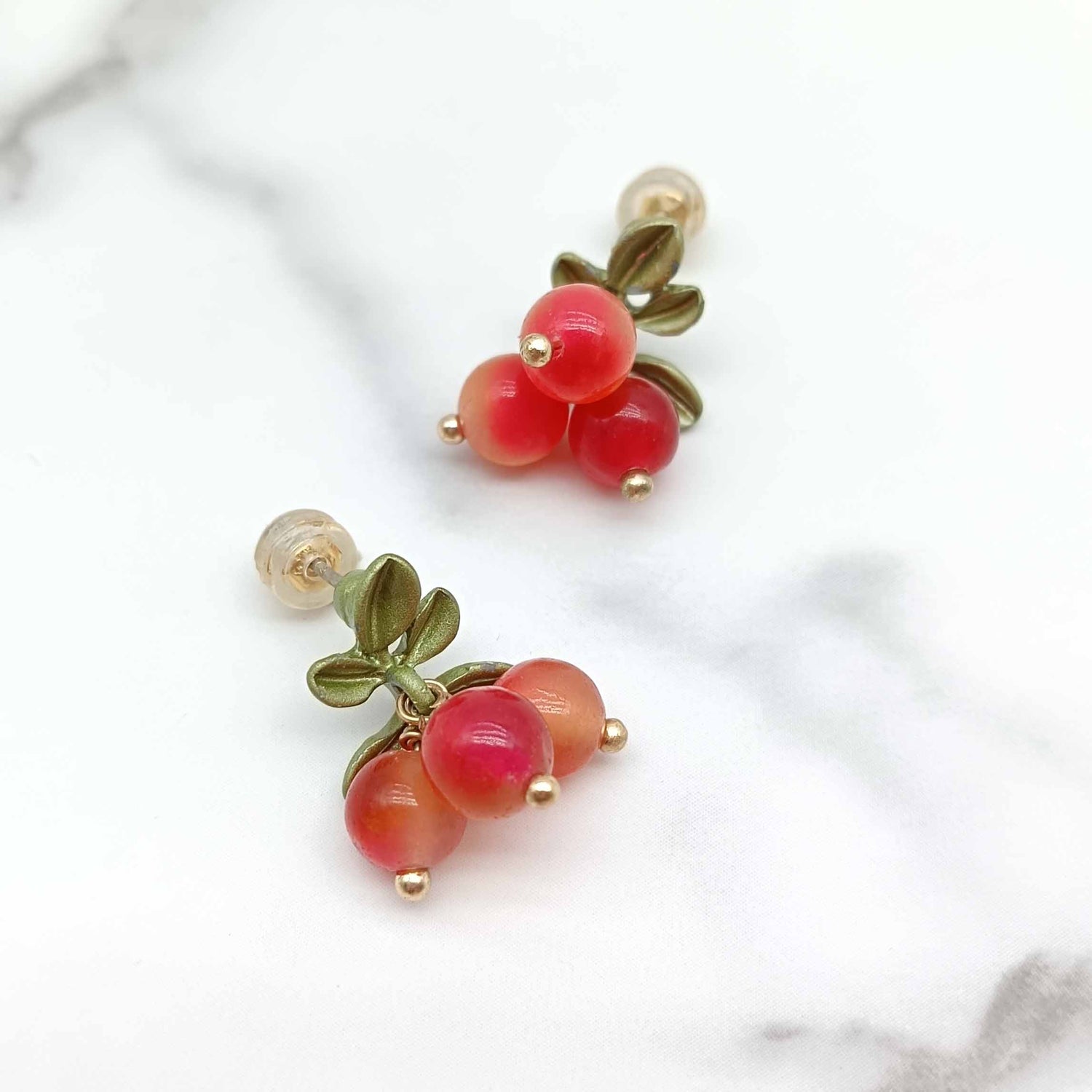 Pair of earrings with red berry-like beads and green leaves on a light background