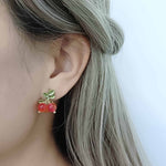 Close-up of an ear wearing cherry-themed earrings with a blurred background