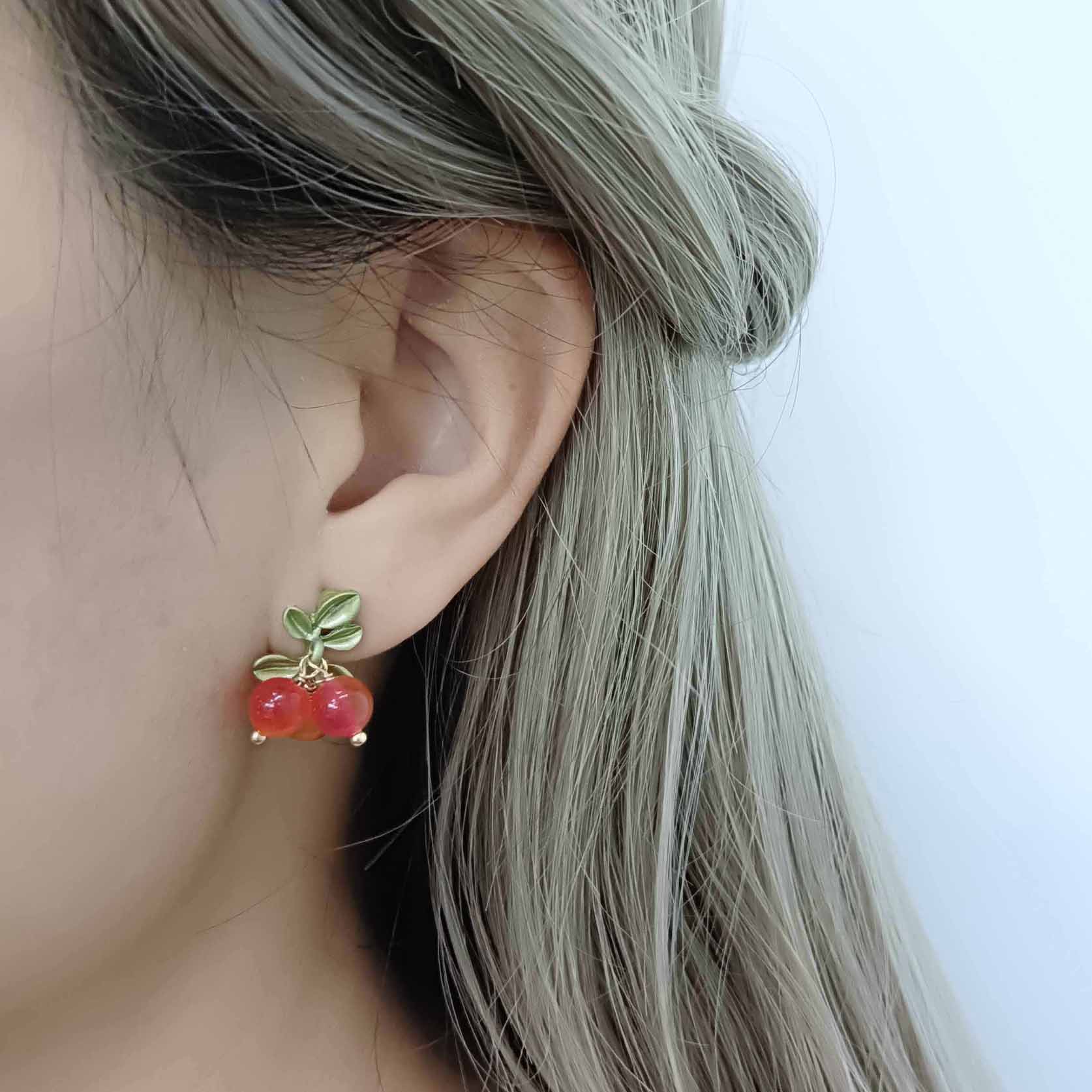 Close-up of an ear wearing cherry-themed earrings with a blurred background