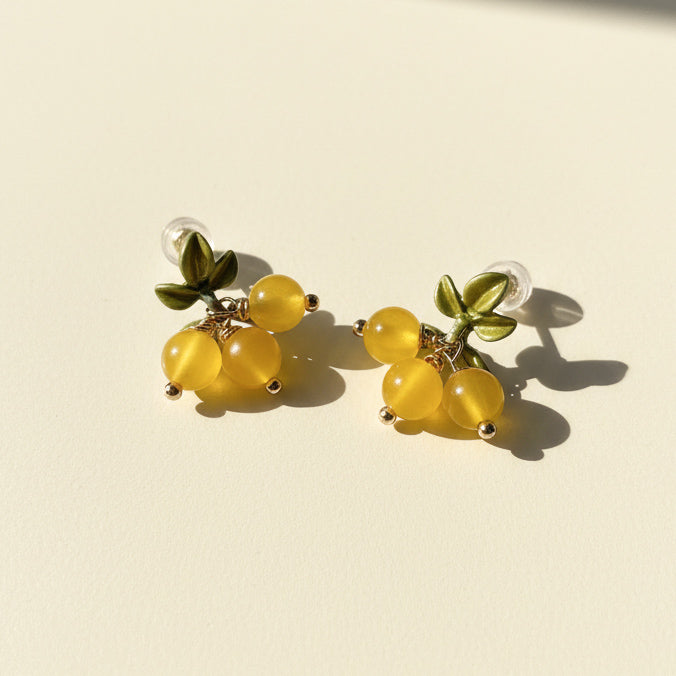 Pair of earrings with yellow beads and green leaves on a beige background