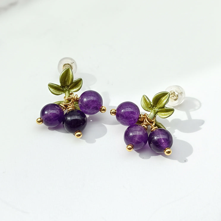 Pair of earrings with purple beads and green leaves on a white background