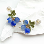 Pair of earrings with blue beads and green leaves on a white shell background