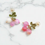 Pair of earrings with pink beads and green leaves on a marble background