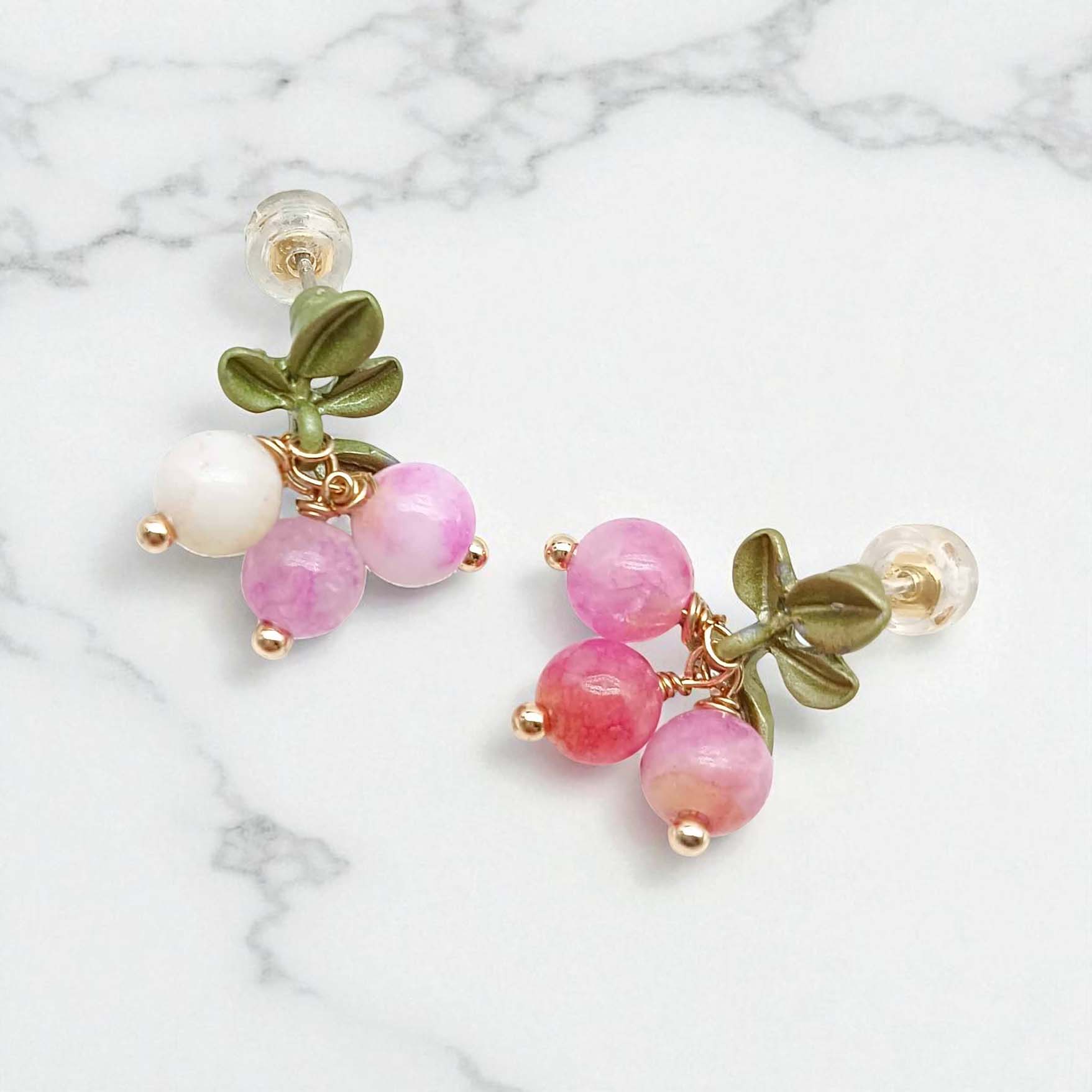 Pair of earrings with pink beads and green leaves on a marble background