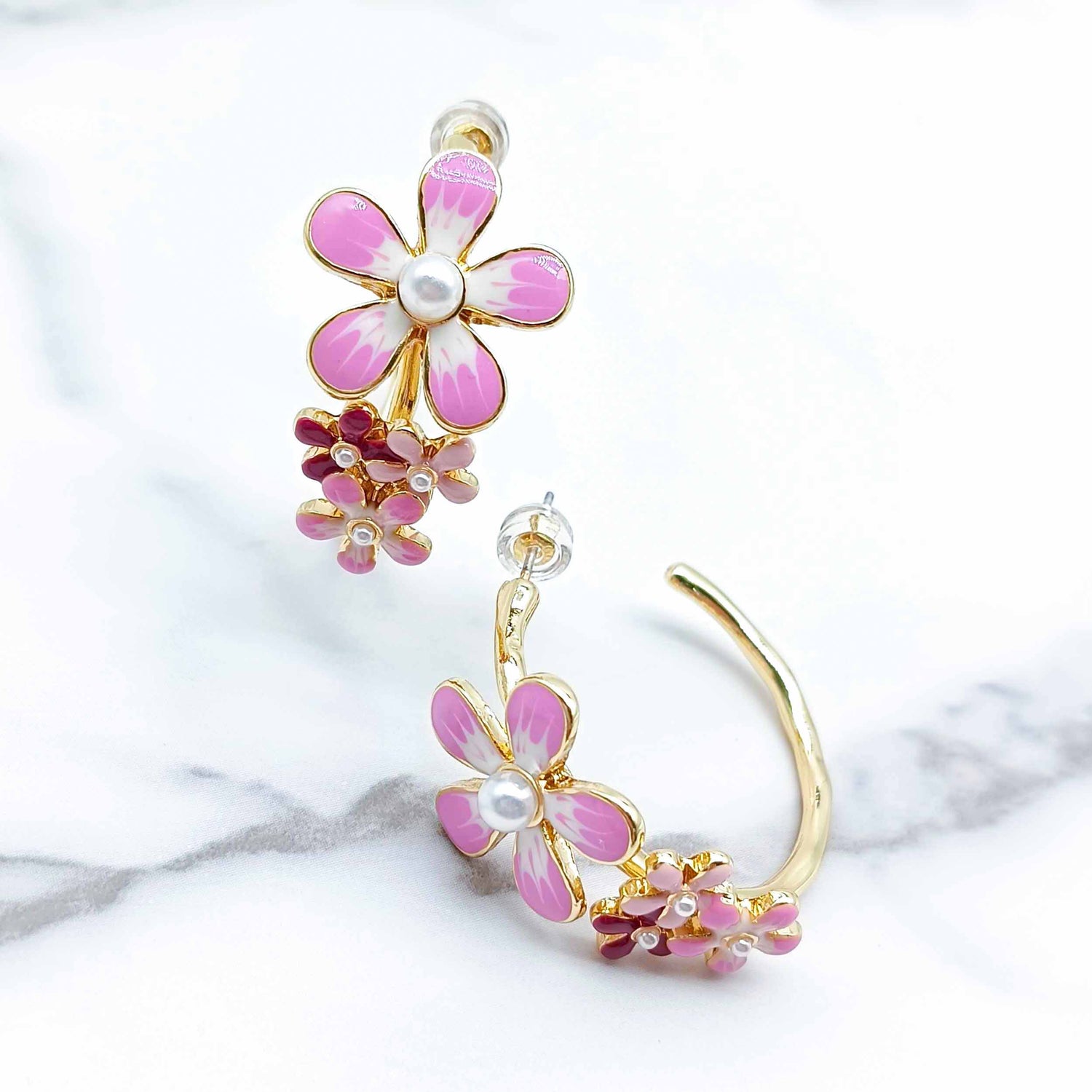 Flower-shaped earrings with pink and gold details on a marble surface
