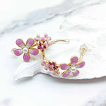 Floral earrings with pink flowers and gold accents on a white shell background