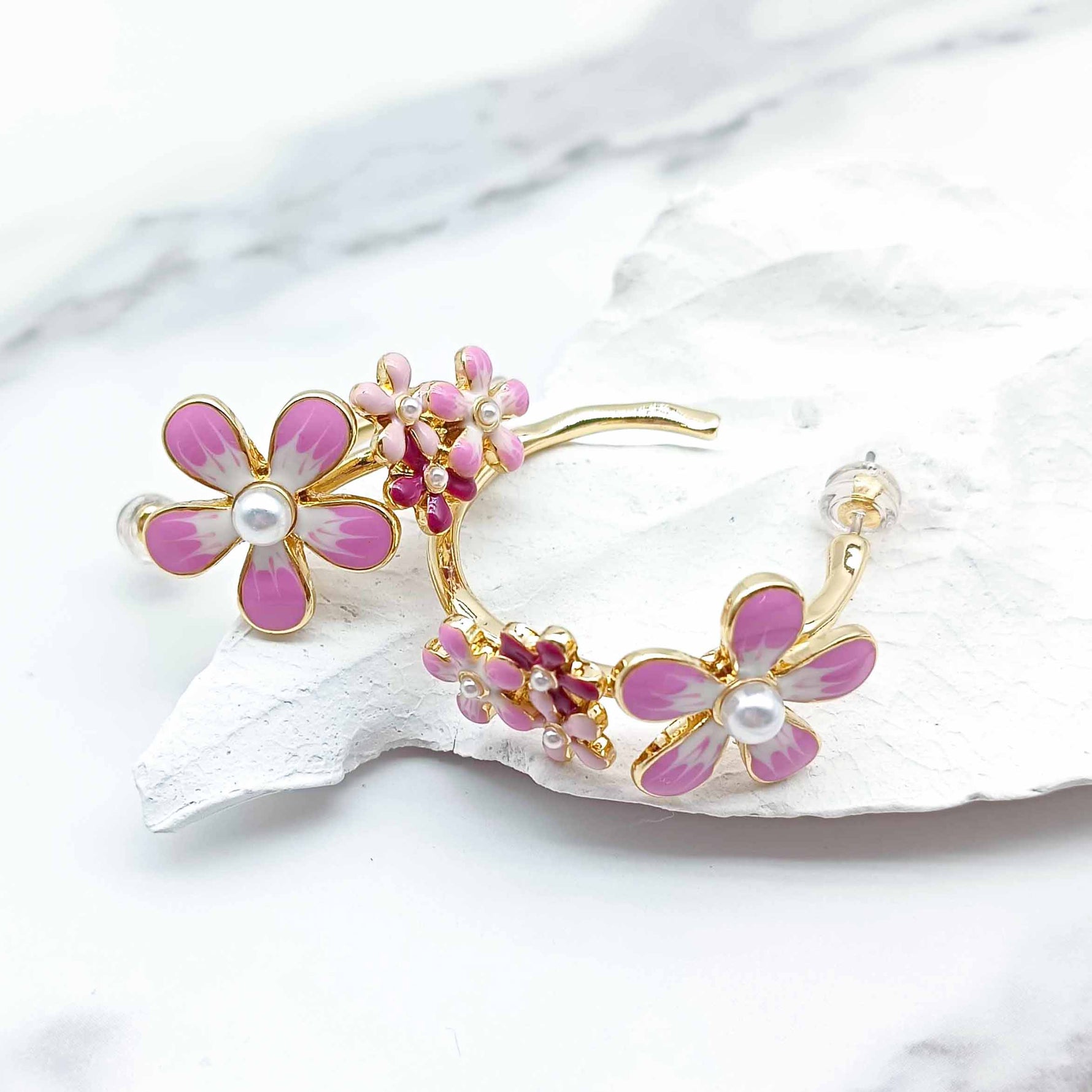 Floral earrings with pink flowers and gold accents on a white shell background