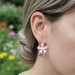 Close-up of a person wearing pink flower earrings with a blurred garden background