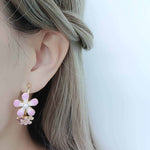 Close-up of an ear wearing a pink flower-shaped earring with a white background