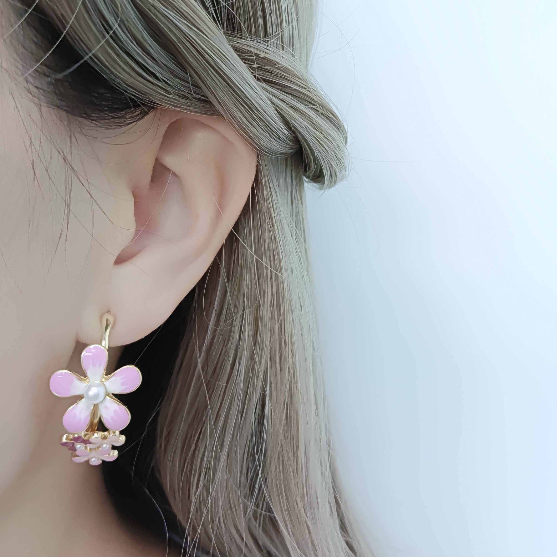 Close-up of an ear wearing a pink flower-shaped earring with a white background