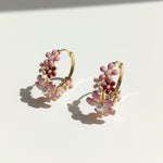 Gold hoop earrings with pink floral and pearl details on a light background