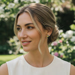 Model wearing green enamel hummingbird stud earrings in garden sunlight, elegant nature-inspired look.