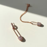 Rose gold safety pin earrings with clear gemstones on a light background