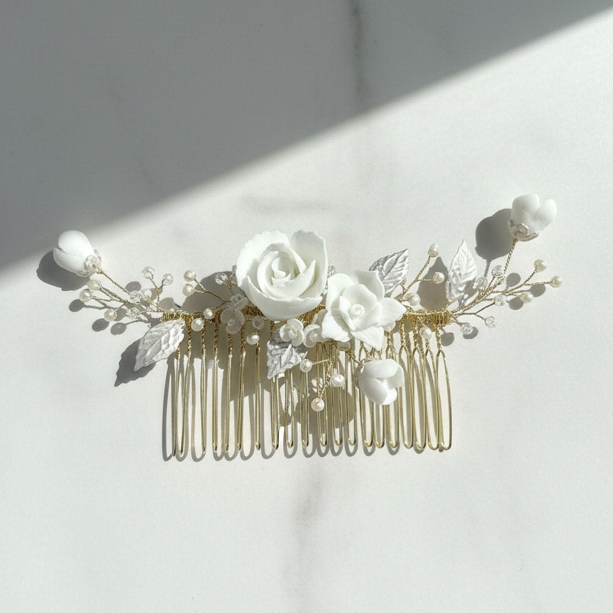 Porcelain floral bridal hair comb with white roses and pearls on marble background.