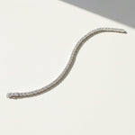 Curved moissanite tennis bracelet displayed on white surface