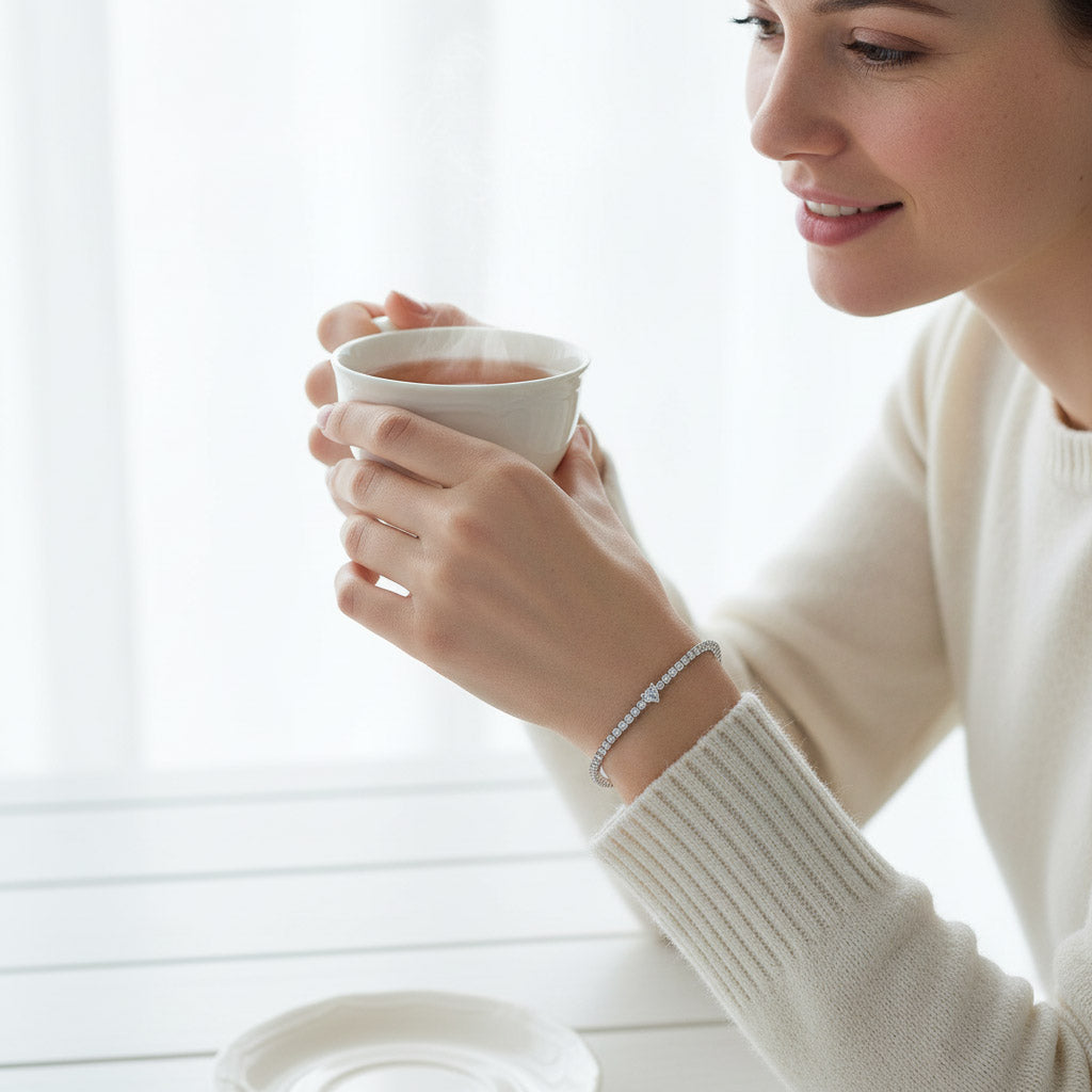 Woman holding a teacup while wearing a white moissanite heart tennis bracelet