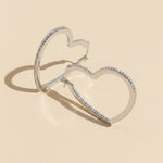 Heart-shaped silver hoop earrings with moissanite on a beige background