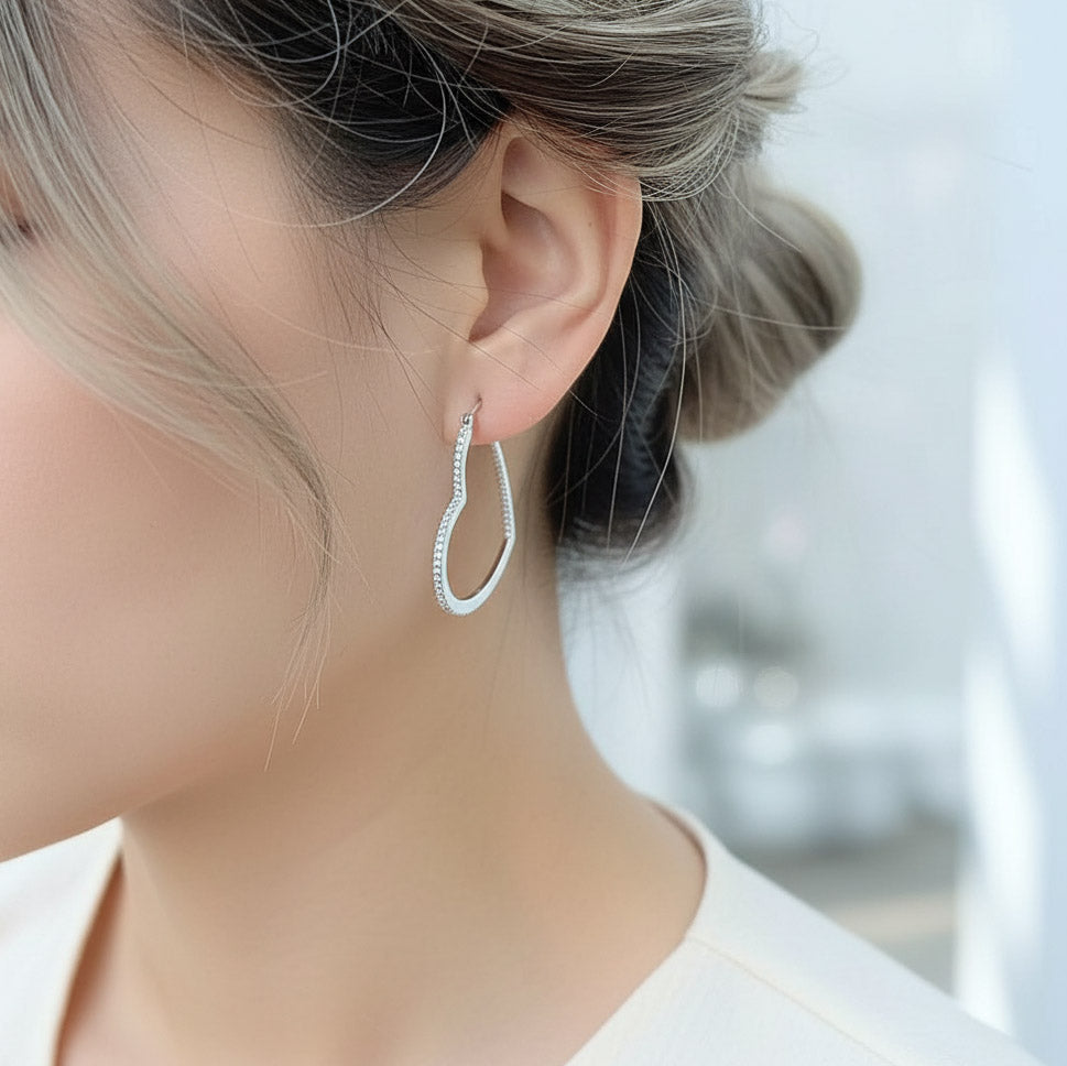 Elegant heart-shaped silver hoop earrings with lab-grown diamonds, worn by mode
