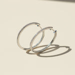 Standing display of 30mm platinum-plated moissanite hoop earrings with full pavé D/VVS1 stones on beige background.