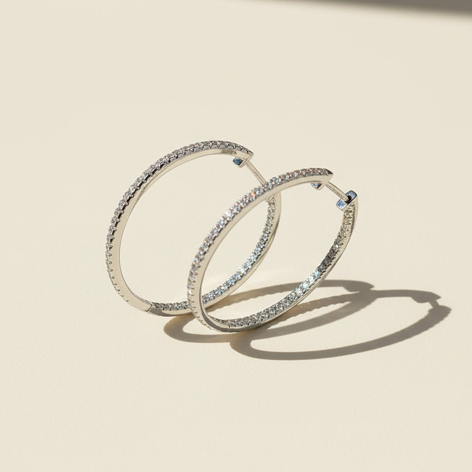 Standing display of 30mm platinum-plated moissanite hoop earrings with full pavé D/VVS1 stones on beige background.