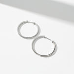 30mm platinum-plated sterling silver moissanite hoop earrings, flat lay on white surface.