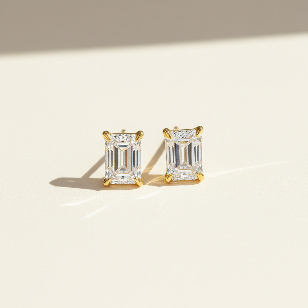 Emerald-cut moissanite stud earrings in platinum plated silver on neutral background.