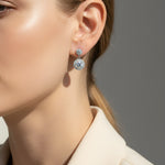 Close-up of a person wearing moissanite halo drop earrings in platinum plated silver against a neutral background