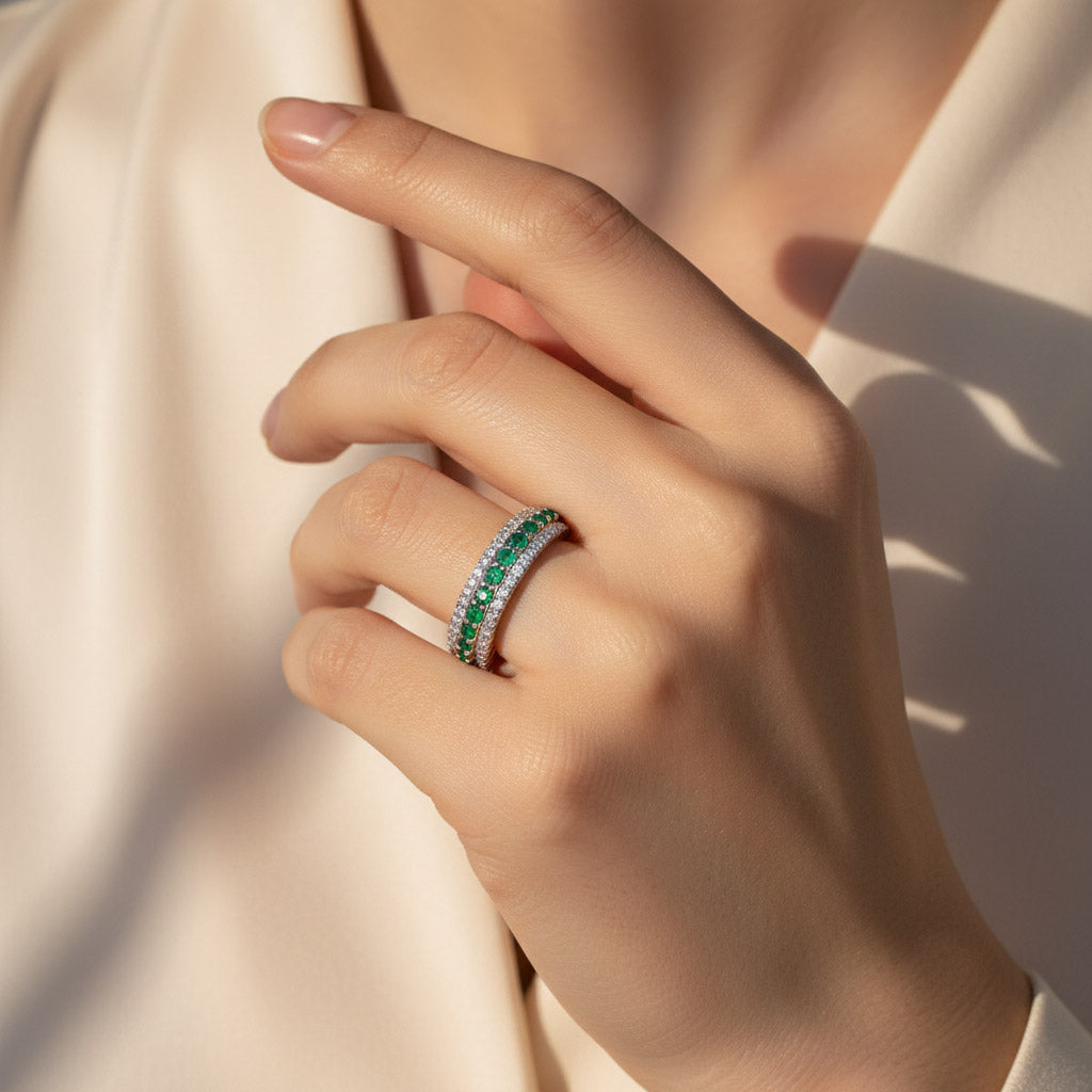 Moissanite eternity ring with emerald stones worn on hand, platinum plated silver band