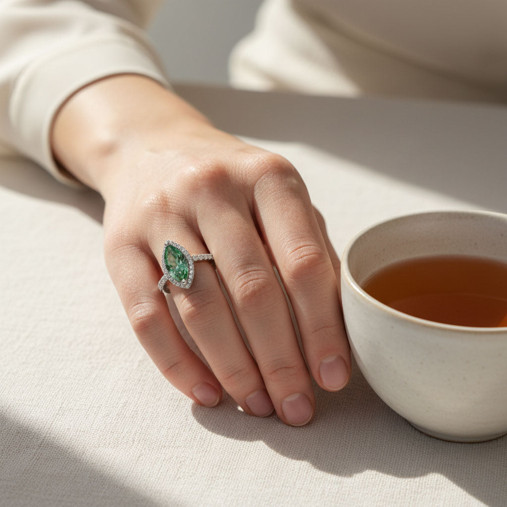 woman wearing green marquise moissanite halo ring elegant statement ring with a cup of tea on a light surface