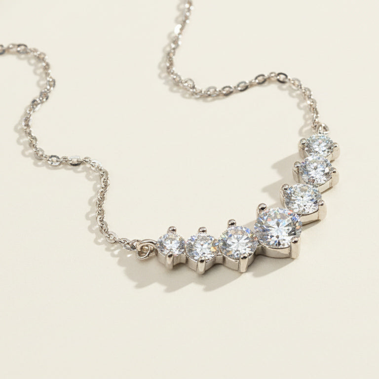 Close-up of platinum-plated silver bar necklace featuring graduated round moissanite stones