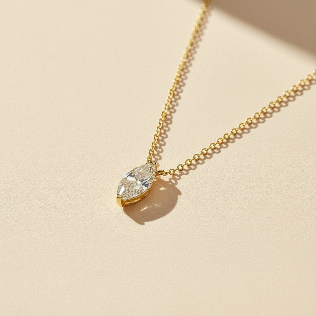 Gold marquise-cut 1ct lab grown moissanite necklace on a soft beige background with sunlight shadow.