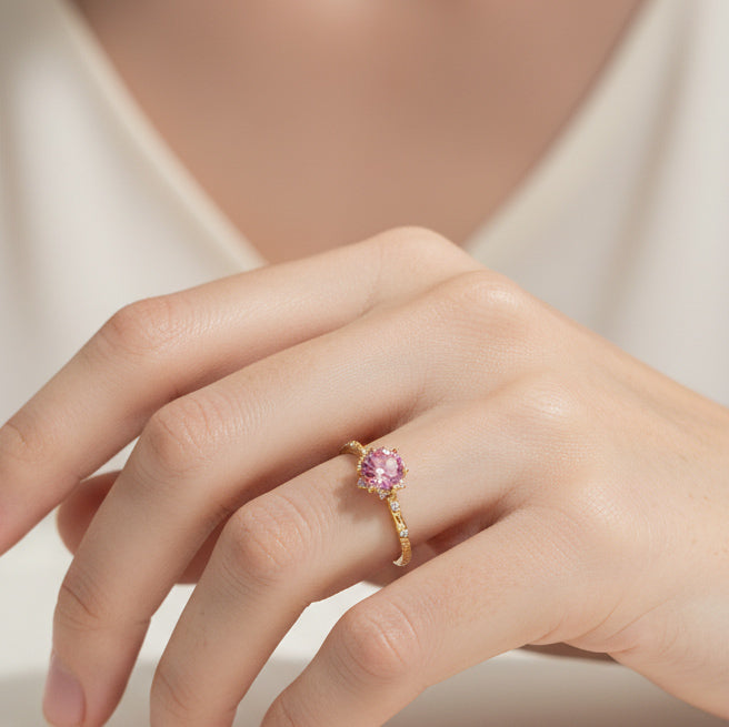 Hand wearing a gold ring with a pink gemstone on a neutral background