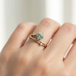 Model hand wearing two-tone lab-grown diamond ring with green gemstone centerpiece