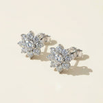Floral moissanite stud earrings photographed in warm sunlight on beige backdrop.