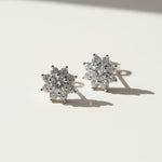 Pair of floral halo moissanite stud earrings on a white background with shadows.