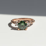 Close-up of green moissanite engagement ring with rose gold band