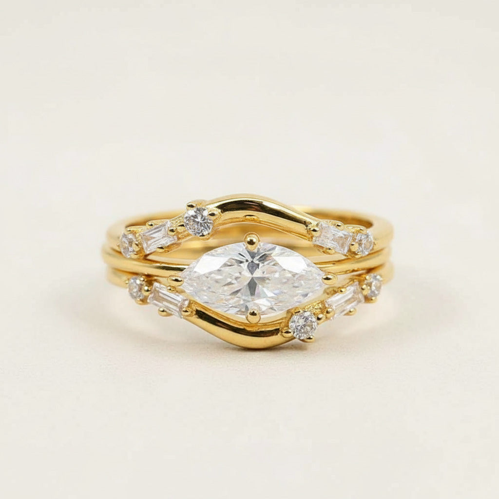 A set of three gold-plated silver rings featuring a marquise-cut moissanite center stone and two matching curved bands adorned with round and baguette-cut accent stones. The stacked design creates a luxurious, layered look with brilliant sparkle and elegant symmetry.