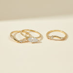 A set of three gold-plated silver rings displayed on a light beige surface. The set includes one ring with a marquise-cut moissanite center stone and two curved bands adorned with round and baguette-cut accent stones. The minimalist, elegant design allows the rings to be worn stacked or separately for a refined look.