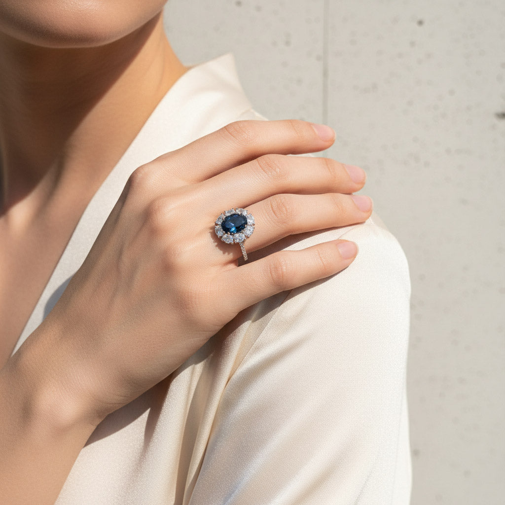 Model wearing oval sapphire blue halo ring in platinum plated sterling silver