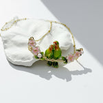 Necklace with green parrot charms and pink flowers on a white stone background