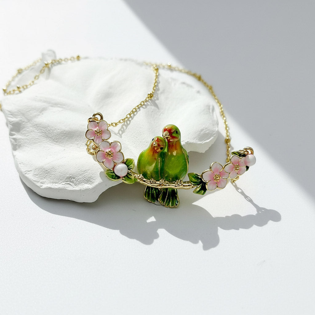Necklace with green parrot charms and pink flowers on a white stone background