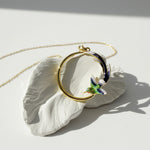 Necklace with a round pendant featuring a colorful bird design, displayed on a white shell against a light background.