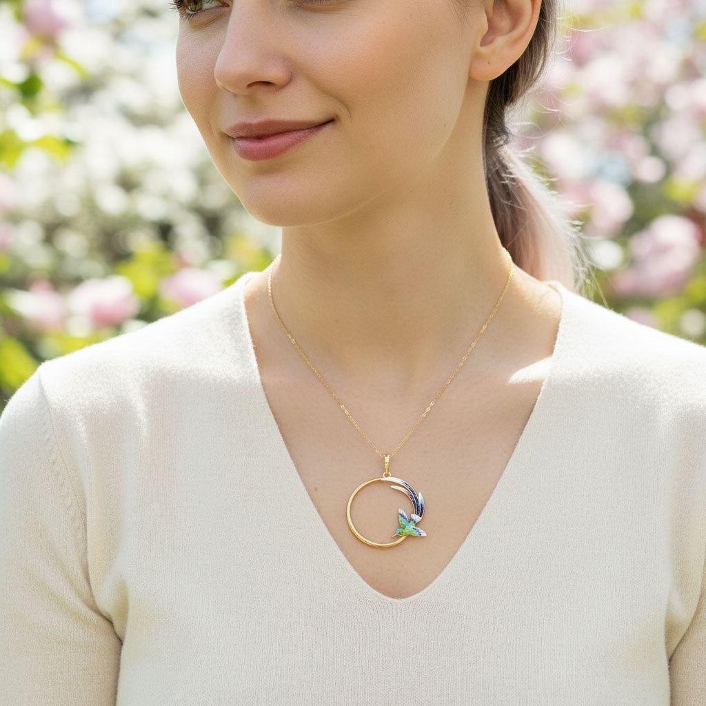 Woman wearing a gold necklace with a colorful pendant against a blurred floral background