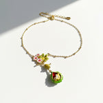 Gold bracelet with green and pink floral charms on a white background
