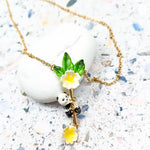 Handcrafted gold-plated necklace featuring a cute panda climbing a bamboo-like branch adorned with green enamel leaves and delicate yellow-and-white flowers, displayed on a textured stone background