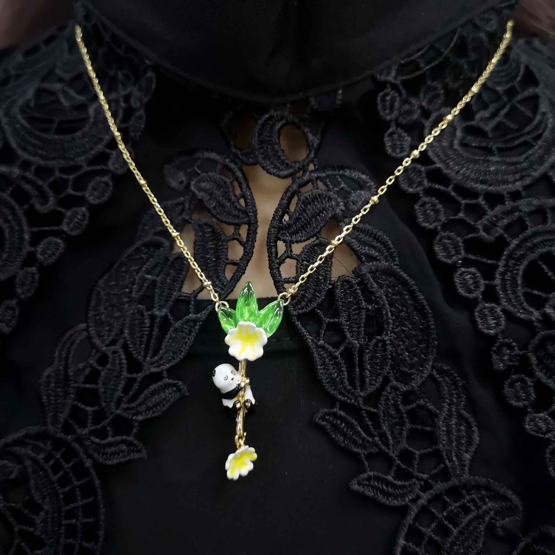 Close-up of a woman wearing a gold-plated panda pendant necklace with green leaf and yellow flower details, styled over black lace clothing.