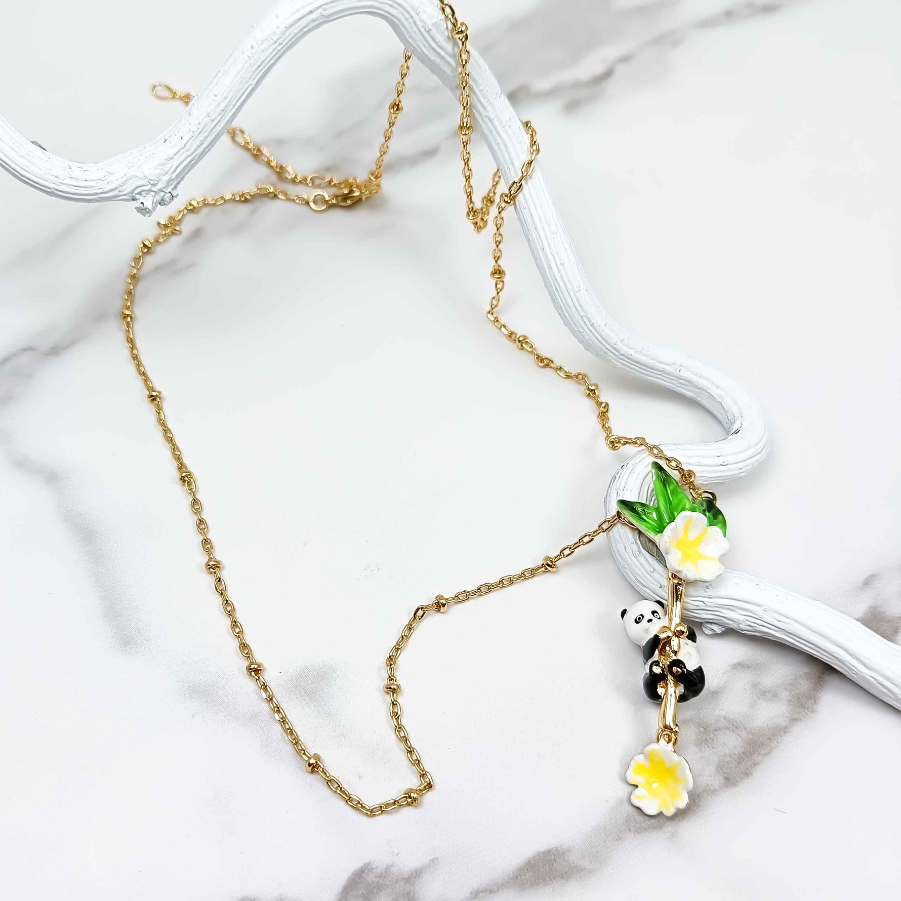 Gold-plated necklace with a handpainted enamel panda pendant hanging over a white marble background.
